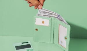 Une main tient un portefeuille avec de l'argent et une calculatrice pour joindre les deux bouts et arrondir ses fins de mois.